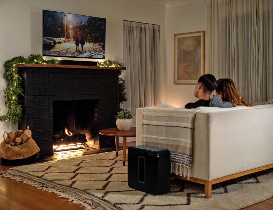 a couple sitting in a living room, watching TV installed over a fireplace