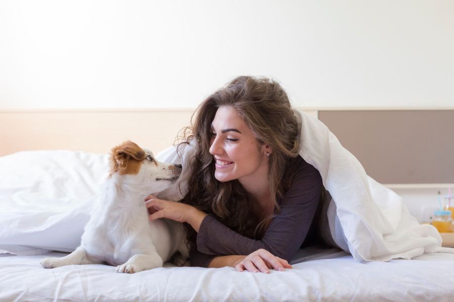 Woman in bed in the morning, smiling at her dog.