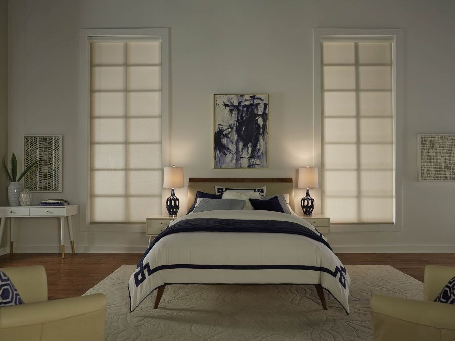 A bedroom with soft lighting and Lutron shades lowered over the windows.
