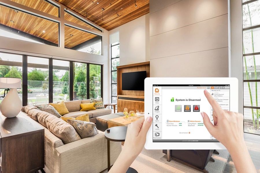 A woman operates her security system on a smart tablet against the backdrop of a modern living area.