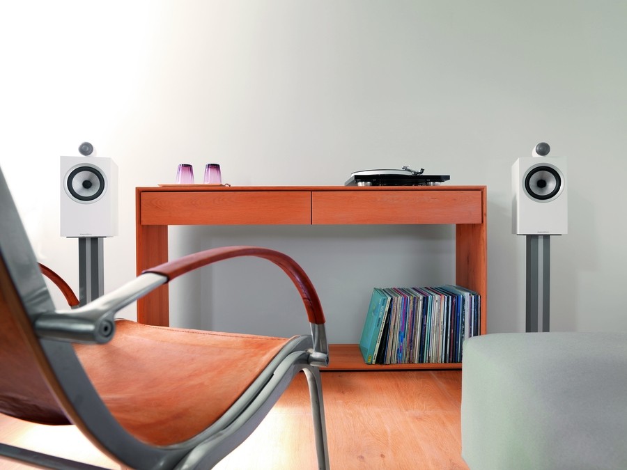 Modern listening room with white bookshelf speakers on stands, a wooden desk holding a turntable, and a vinyl record collection beneath.